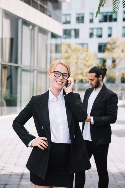 Happy young woman standing in front of her colleague talking on cell phone