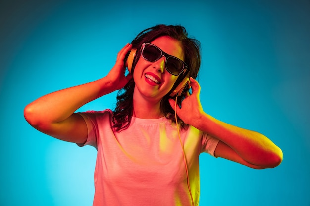 Free photo happy young woman standing and smiling in sunglasses over trendy blue neon studio