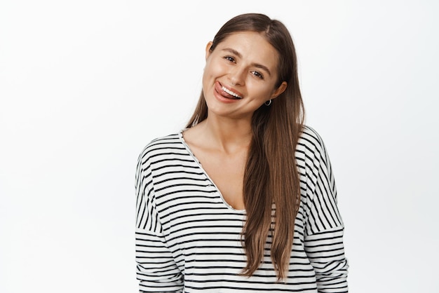 Happy young woman stick tongue and smiling showing white healthy teeth standing in striped blouse against white background