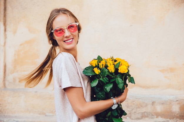 Free photo happy young woman in sunglasses holds a bouquet of yellow roses, posing at camera