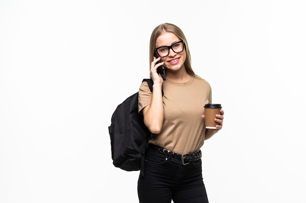 Happy young woman university student with backpack and books talking on cell phone isolated on white surface