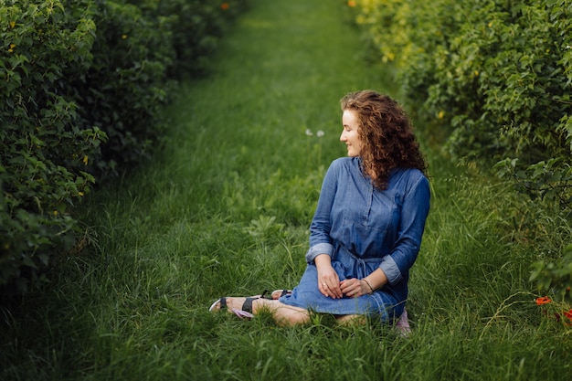 Free Photo happy young woman with brown curly hair, wearing a dress, posing outdoors in a garden