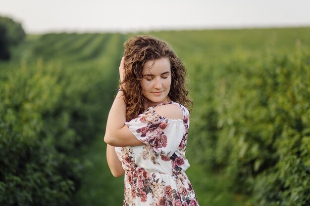 Happy young woman with brown curly hair, wearing a dress, posing outdoors in a garden