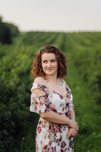 Happy young woman with brown curly hair, wearing a dress, posing outdoors in a garden