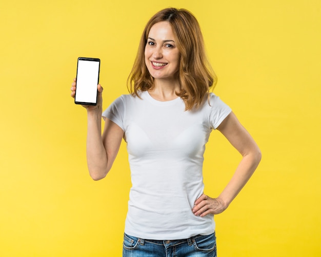 Happy young woman with hands on her hip showing mobile phone with white display screen