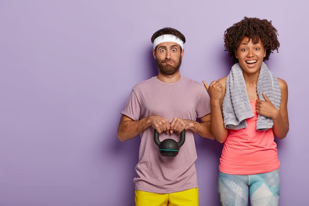 Free photo happy young woman with towel on shoulders points at husband who has surprised expression