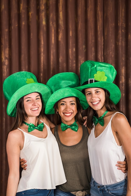 Free photo happy young women in saint patricks hats hugging near wall