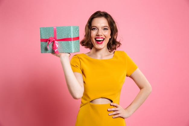 Happy ypung woman with  hand on her waist holding gift box, 