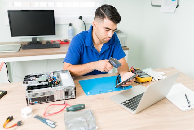 Hardworking technician scanning the barcode of an old broken component to look for a replacement part at the repair shop