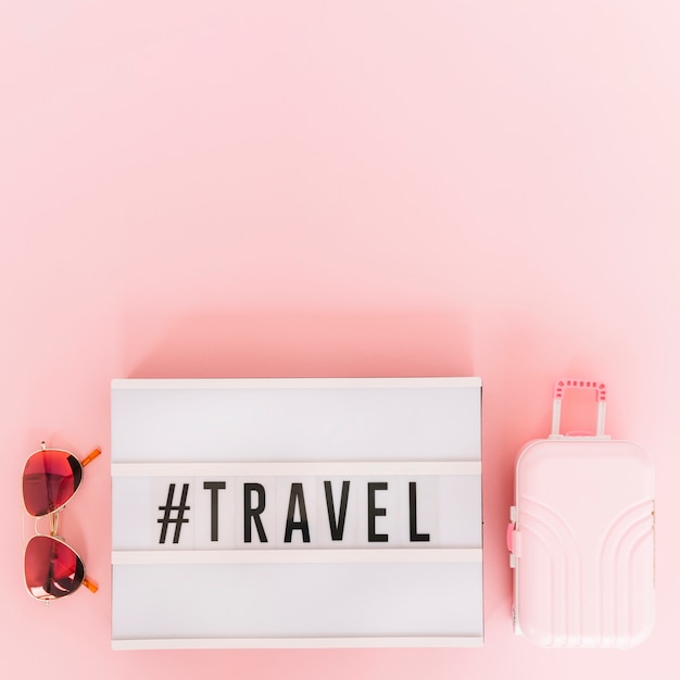 Free Photo hashtag with travel text on lightbox with sunglasses and miniature travel bag on pink background