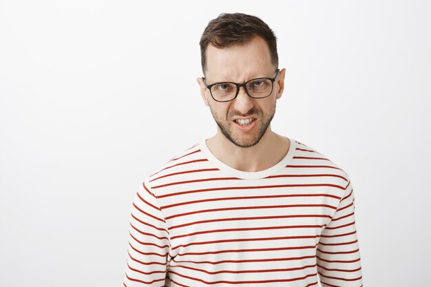 Hate you with all heart. Portrait of outraged disdaining european guy in black glasses, looking from under forehead and frowning, showing teeth in anger