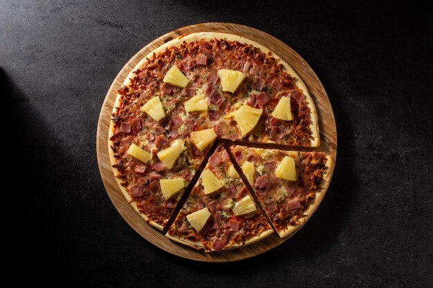 Hawaiian pizza with pineappleham and cheese on black slate background