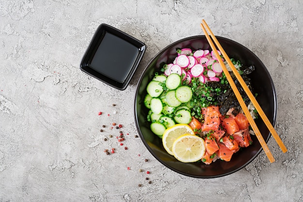 Free photo hawaiian salmon fish poke bowl with rice, radish,cucumber, tomato, sesame seeds and seaweeds. buddha bowl. diet food. top view. flat lay