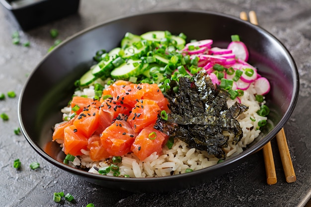 Free photo hawaiian salmon fish poke bowl with rice, radish,cucumber, tomato, sesame seeds and seaweeds. buddha bowl. diet food