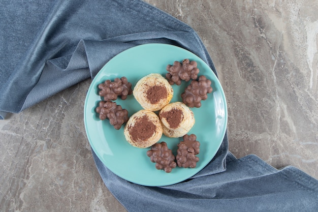 Hazelnut chocolate and cocoa powder on cookies on a plate on towel on blue.