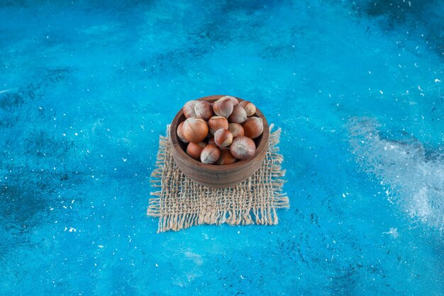 Hazelnuts in a bowl on texture on the blue surface