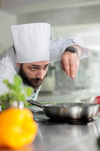 Head chef garnishing delicious gourmet dinner dish with parmesan cheese in restaurant kitchen. Caucasian food industry worker cooking with fresh herbs and organic vegetables.