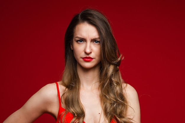 Head shot of young displeased serious female frowning on red studio background with copy space for advertising