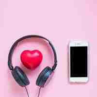 Free photo headphone around the red heart shape and smartphone against pink backdrop