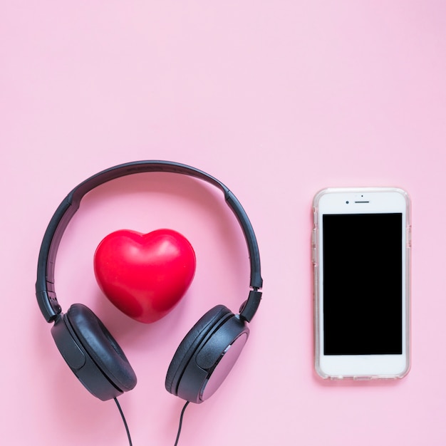 Headphone around the red heart shape and smartphone against pink backdrop