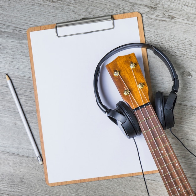 Free photo headphone over the guitar headstock over the white paper on clipboard with pencil