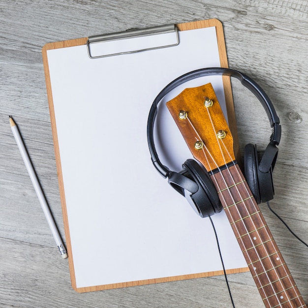 Free Photo headphone over the guitar headstock over the white paper on clipboard with pencil