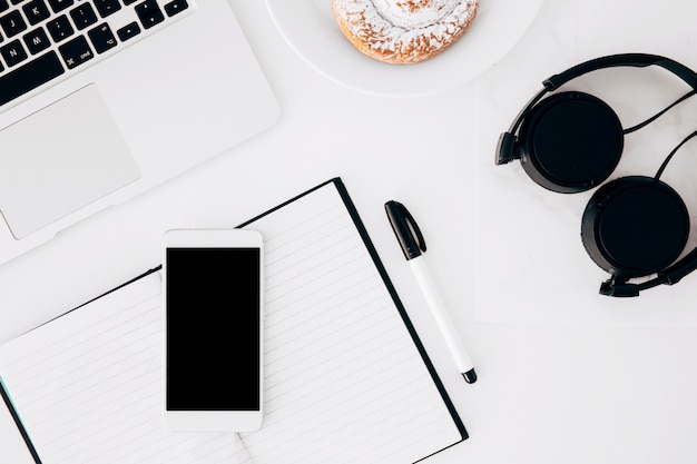 Headphone; laptop; mobilephone; diary; pen and baked food on white background