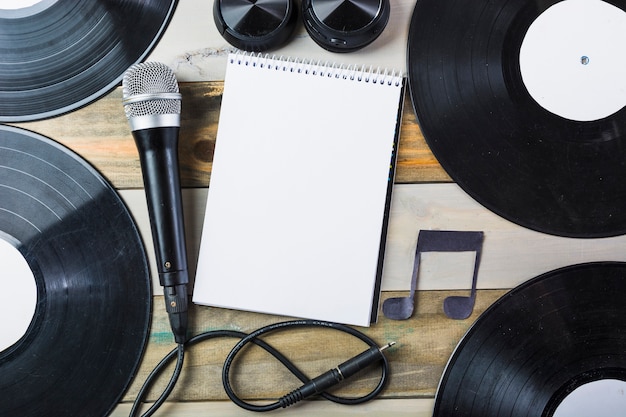 Headphone; microphone; vinyl record and blank spiral notepad with musical note on wooden table