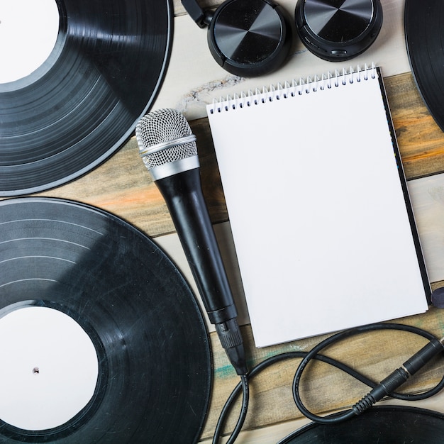 Headphone; microphone; vinyl record and blank spiral notepad on wooden table