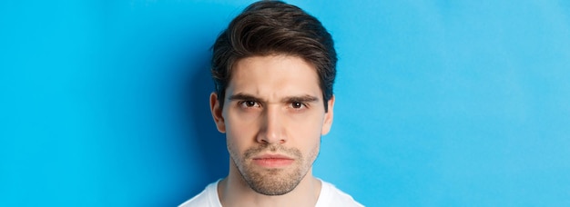 Free photo headshot of angry man frowning looking disappointed and bothered standing over blue background