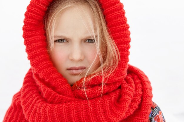 Headshot of beautiful blonde Caucasian little girl wearing red woolen scarf around head and neck