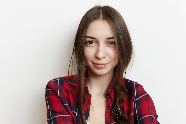 Free Photo headshot of cute european woman in love can't stop smiling, looking with happy joyful expression on her face. beautiful young woman dressed in casual checkered shirt having rest indoors