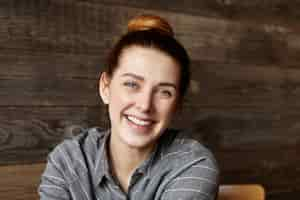 Free photo headshot of cute girl with hair bun spending lunch break at restaurant with wooden walls