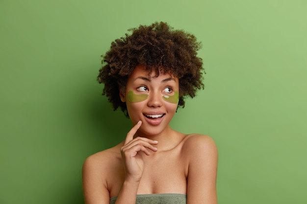 Headshot of dreamy thoughtful healthy woman with Afro hair enjoys skin care procedures