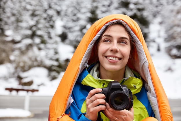 Free Photo headshot of glad female traveler recreats in snowy mountains, makes photos of scenic view, poses against winter space, smiles gently