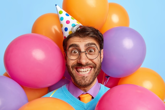 Headshot of handsome joyful guy surrounded by party balloons posing