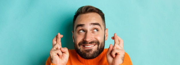 Free photo headshot of hopeful bearded man making a wish smiling and holding fingers crossed for good luck stan