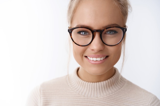 Headshot of hopeful dreamy attractive elegant woman in trendy glasses with combed hair smiling looking friendly and amused at camera having fun expressing positive emotions against white background