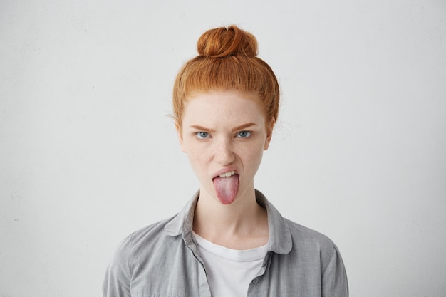 Free Photo headshot of naughty girl of european appearance sticking out tongue, trying to tease someone, looking immature and offensive, all her appearance expressing rudeness and disgust. signs, symbols