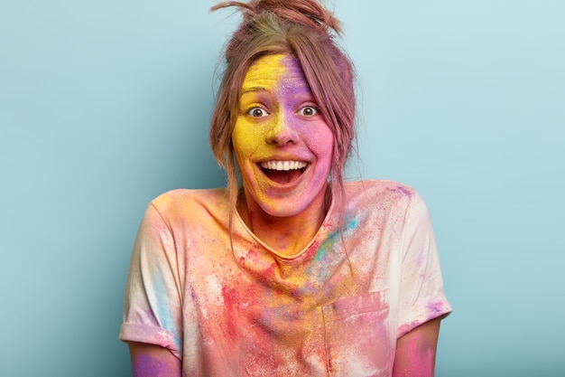 Free photo headshot of optimistic woman plays with colors on holi festival, dressed in white t shirt