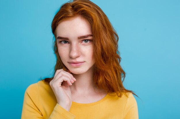 Headshot Portrait of happy ginger red hair girl with freckles smiling looking at camera. Pastel blue background. Copy Space.