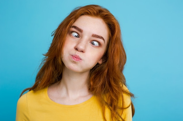 Free photo headshot portrait of happy ginger red hair girl with funny face looking at camera. pastel blue background. copy space.