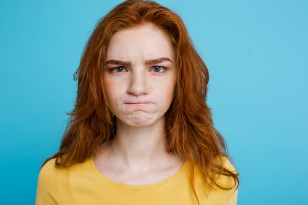 Free photo headshot portrait of tender redhead teenage girl with serious expression looking at camera. caucasian woman model with ginger hair posing indoors.pastel blue background. copy space.