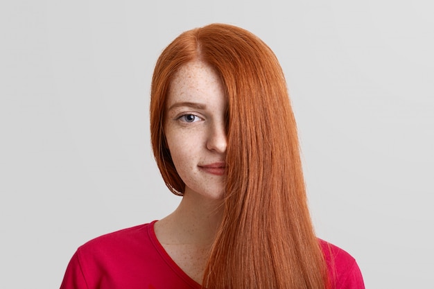 Headshot of pretty young ginger female model covers half of face with her straight luxurious hair