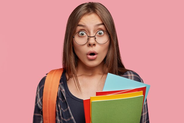 Headshot of stunned student posing against the pink wall with glasses