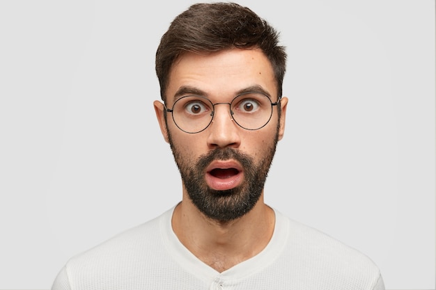 Headshot of stunned young European guy with thick stubble, stares at camera