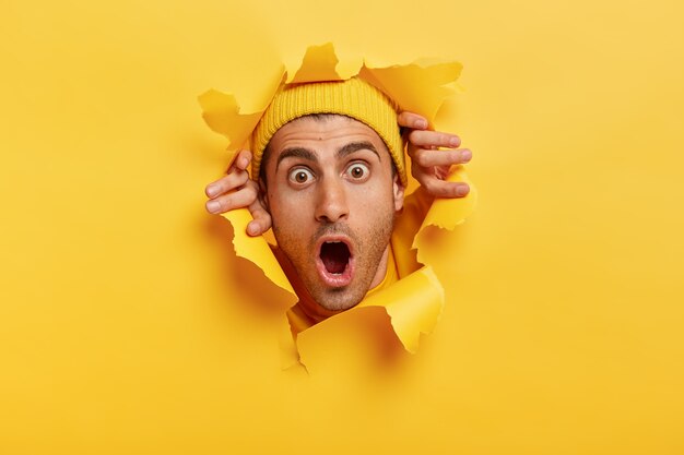 Headshot of stupefied young man with European appearance, wears yellow hat