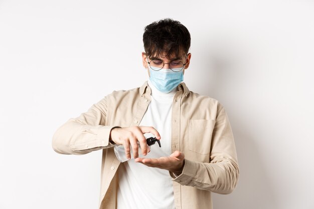 Health covid and quarantine concept young hispanic guy in glasses and face mask using hand sanitizer...