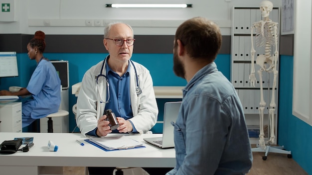 Free photo health specialist explaining disease treatment to patient in cabinet, showing bottle of prescription medicine pills. flask with painkillers, drugs and medication to cure health care disease.