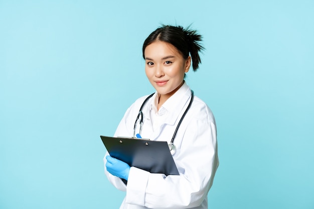 Healthcare and clinic concept smiling korean doctor woman physician in medical uniform holding clipb...